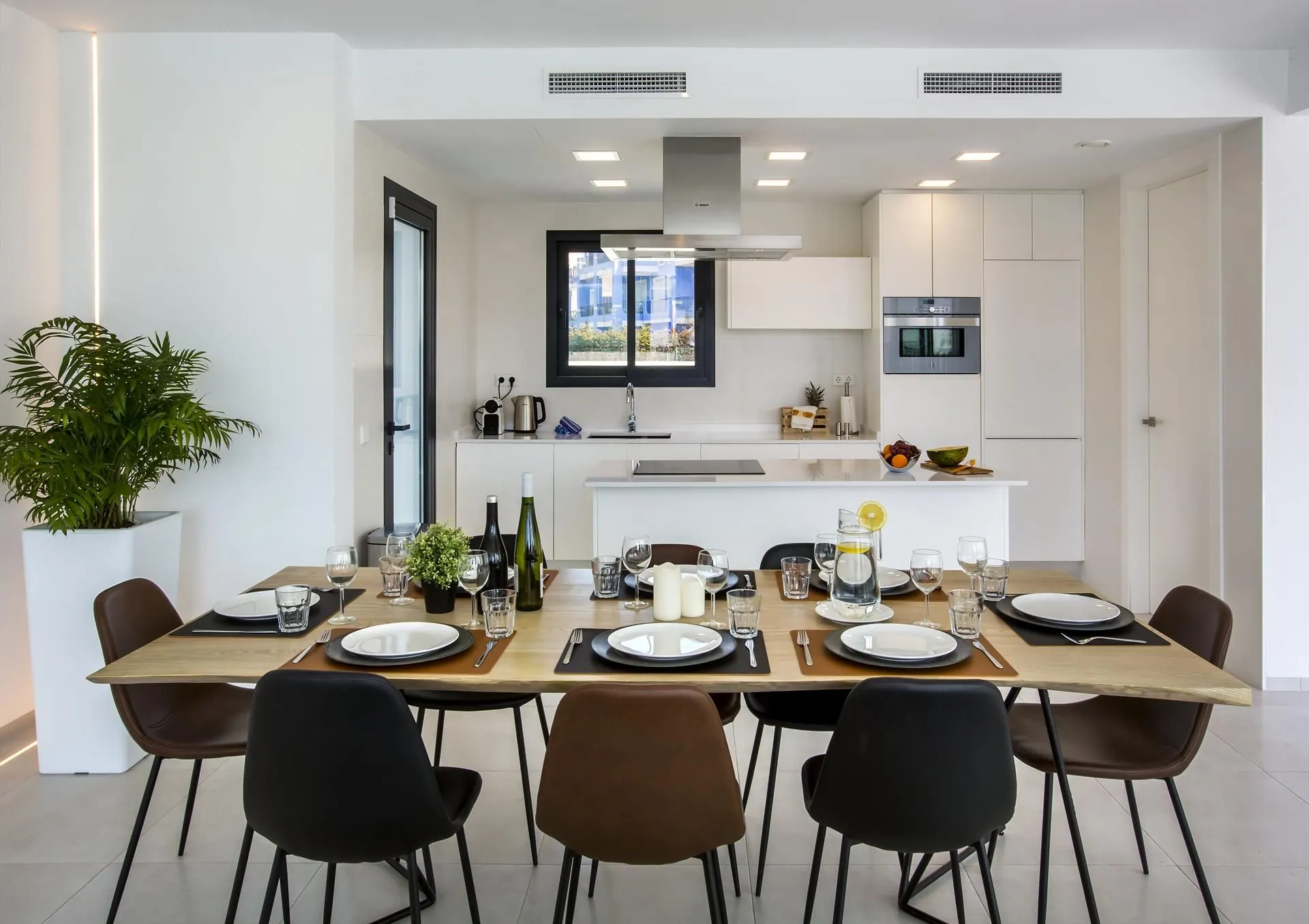 Keuken en eettafel in één ruimte: witte grepenloze kasten en een gedekte tafel met donkere stoelen.