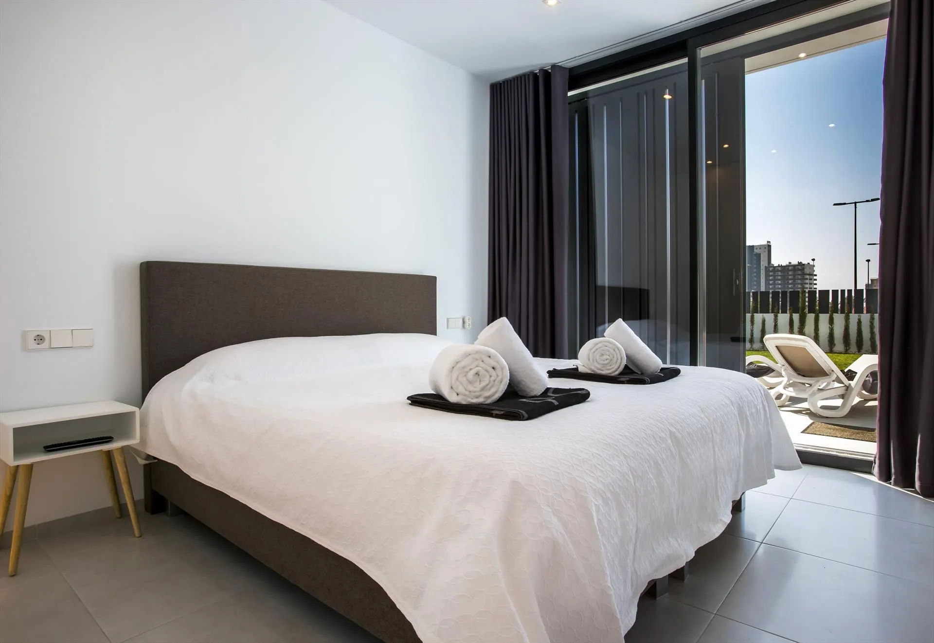 Een slaapkamer met tweepersoonsbed, donker hoofdbord en een schuifdeur naar een terras.